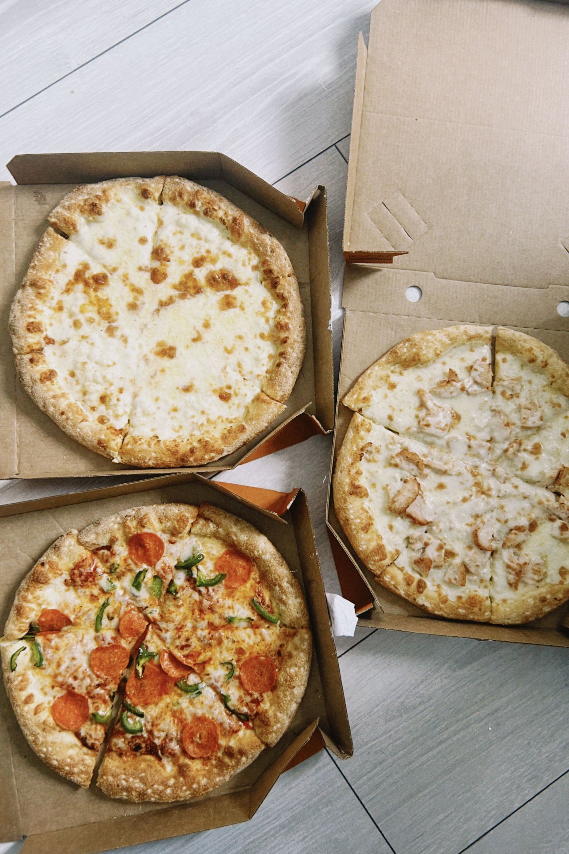 Top view of assorted pizzas in cardboard boxes on a wooden floor, ready to eat.
